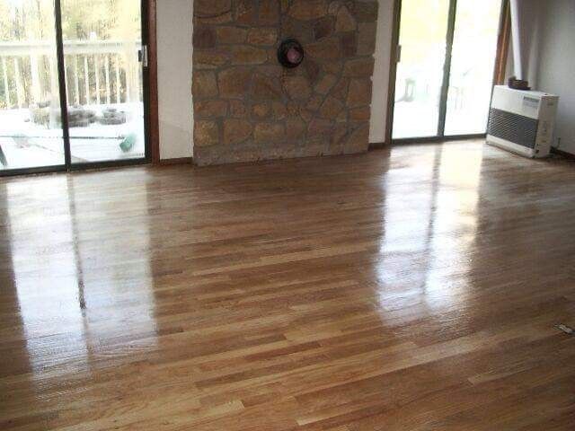 Shiny hardwood floor in a room with large windows and a stone fireplace.