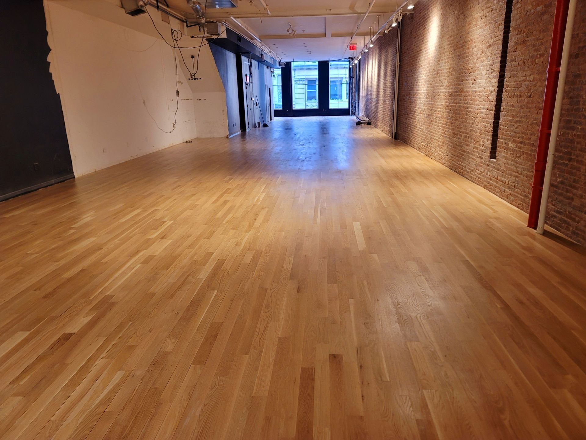 Empty room with wooden floor, exposed brick wall on the right, and a doorway at the far end.