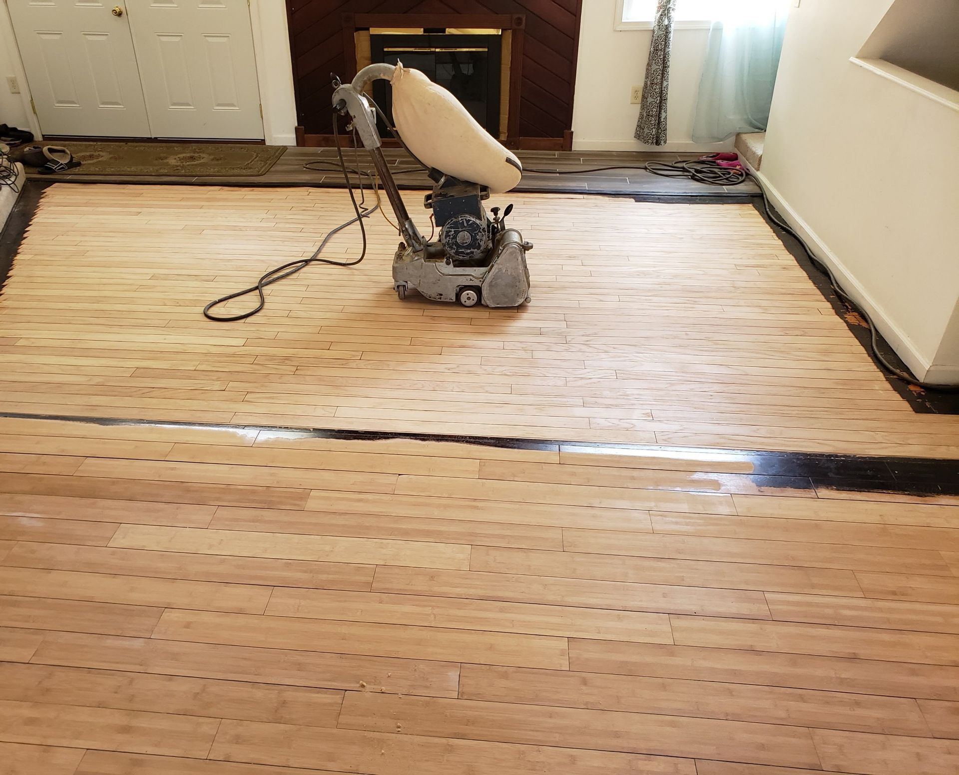 Floor sander on a hardwood floor, next to a fireplace, room under renovation.