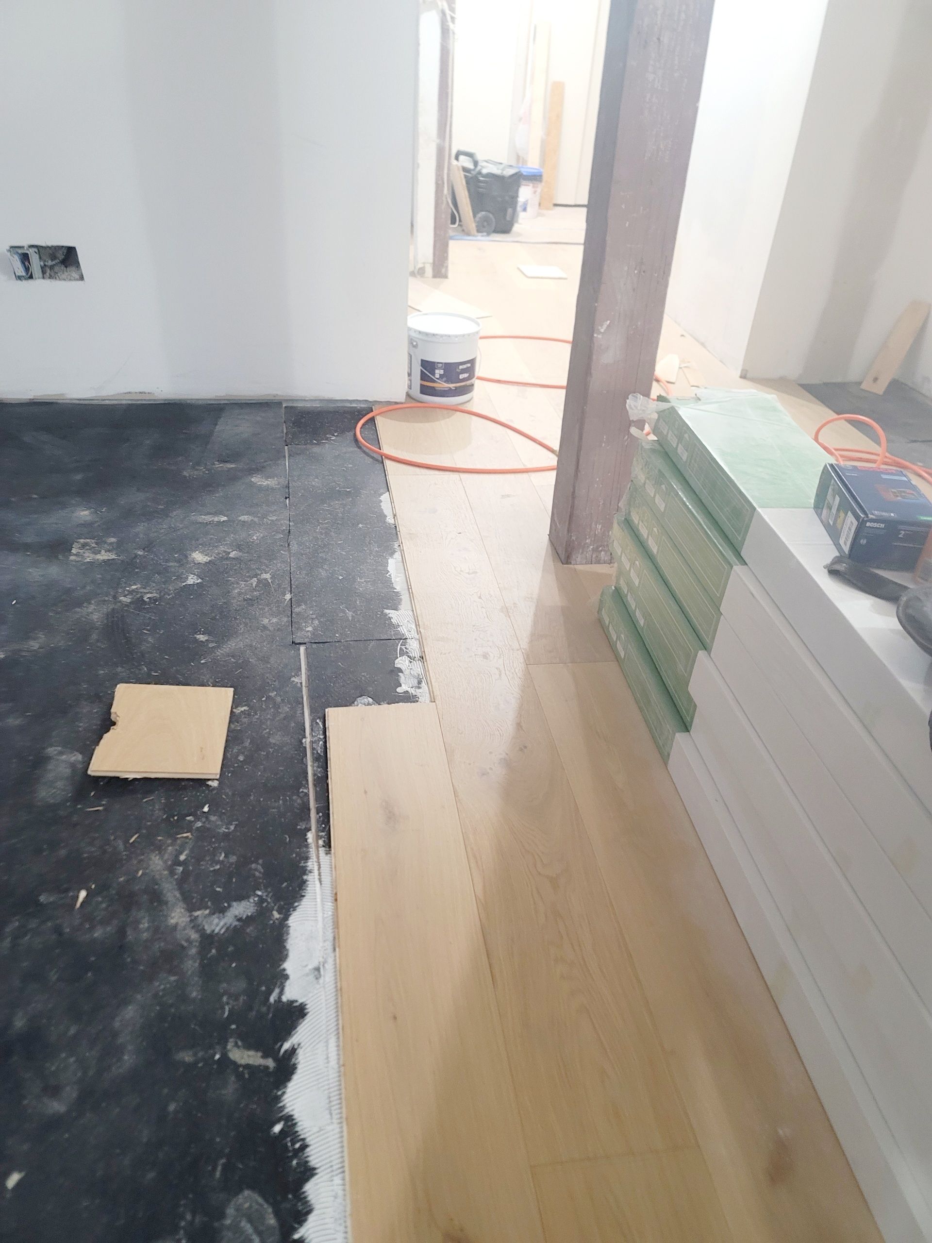 Flooring installation in progress: light wood planks being laid over a dark, uneven surface.