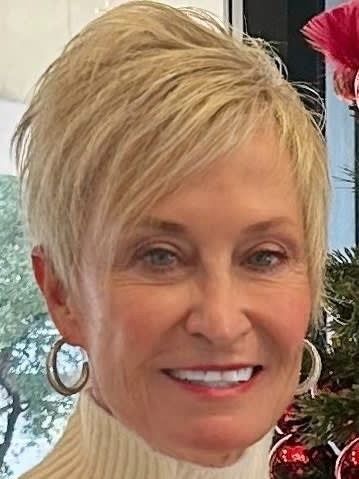 Smiling person with short blonde hair and silver hoop earrings, wearing a red top indoors