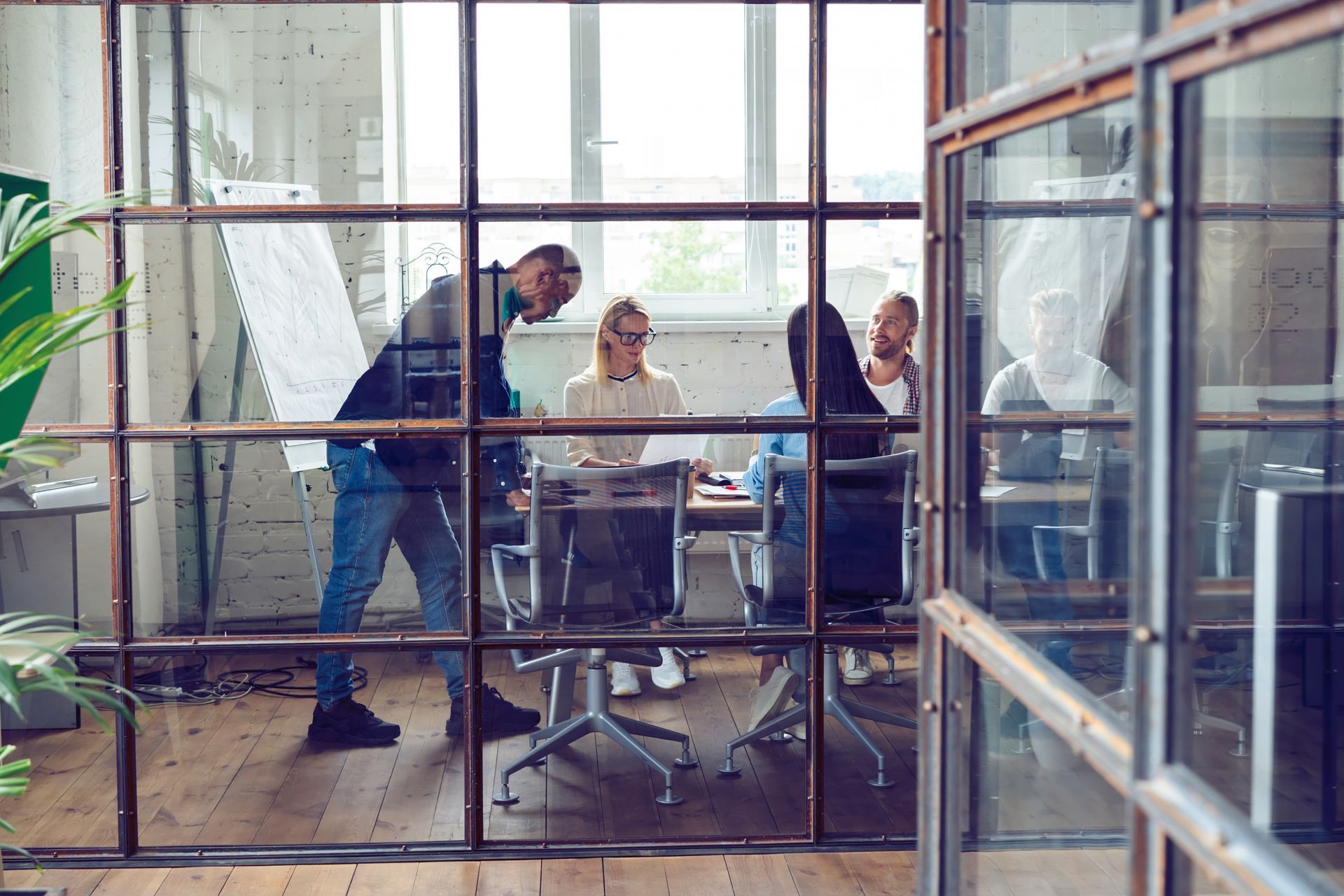People gathered around a table in a bright glass-walled office, discussing documents.