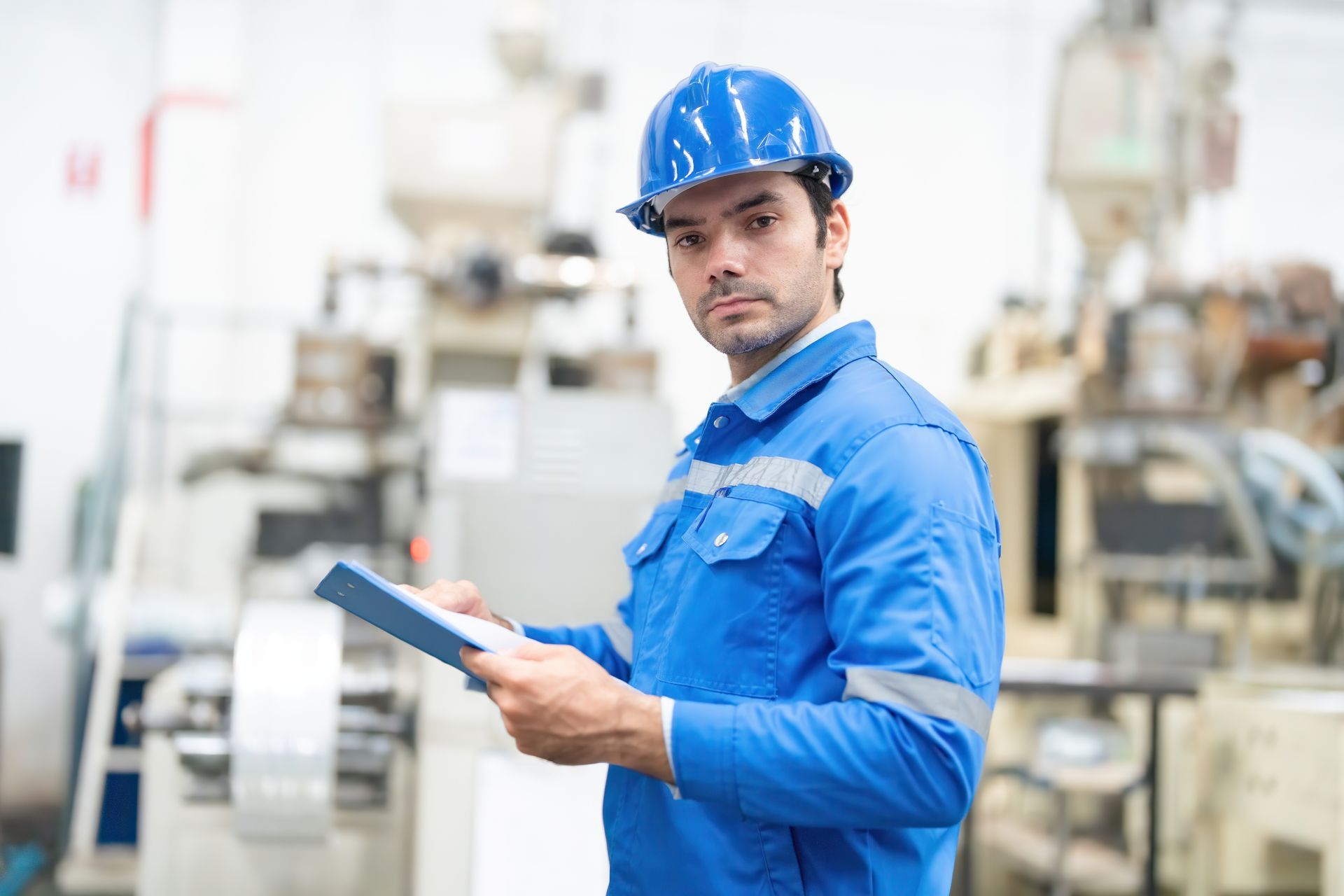 Factory worker in blue hard hat holding a clipboard in an industrial facility
