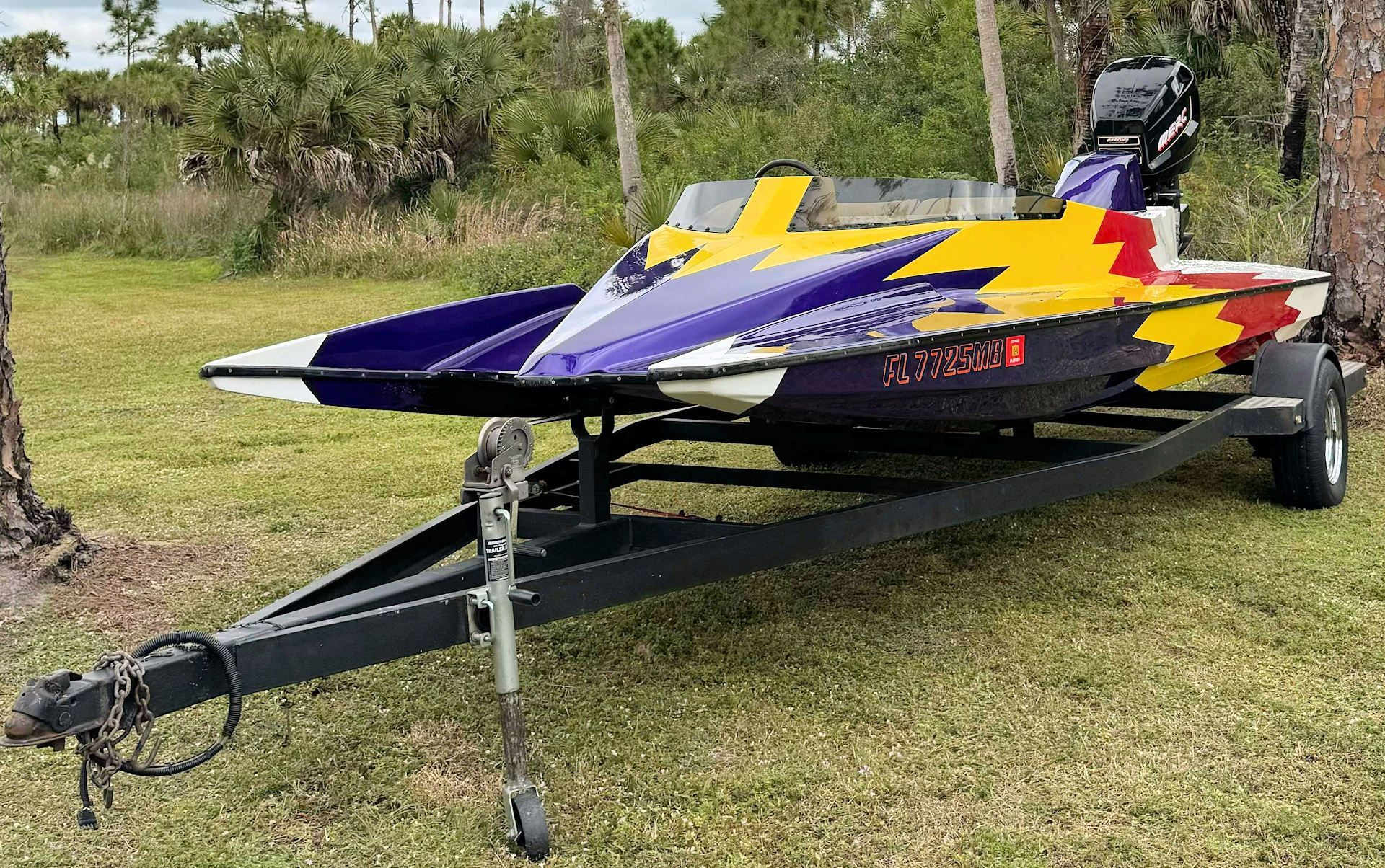 A colorful boat is parked on a trailer in a grassy field.