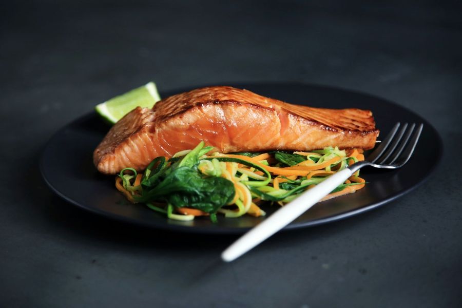 A black plate topped with salmon and vegetables with a fork.