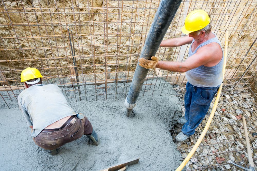 Two construction workers are pouring concrete into a hole.