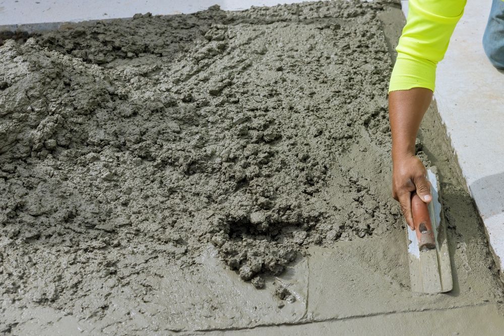 A person is spreading concrete on the floor with a trowel.