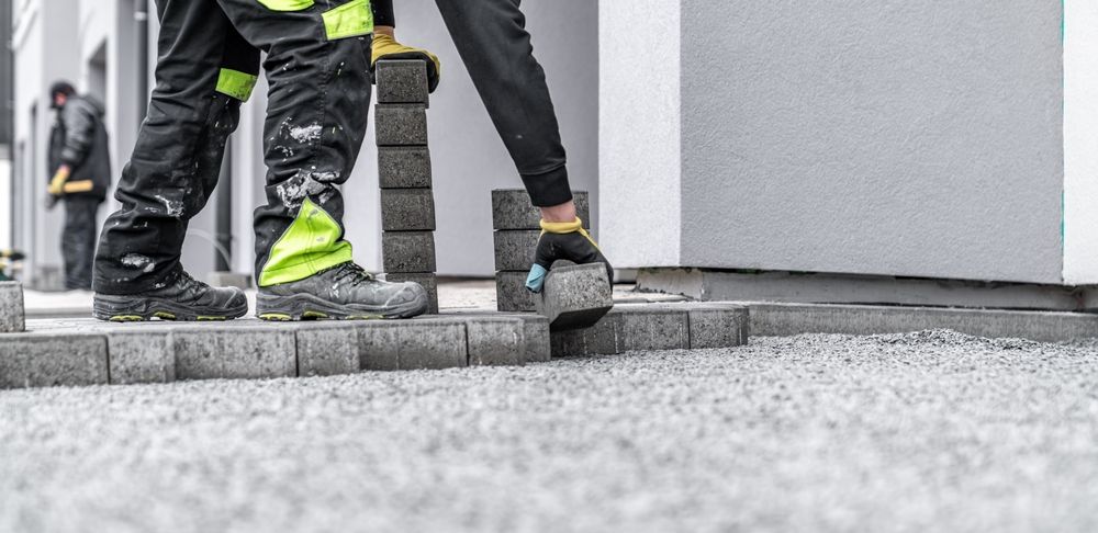 A man is laying bricks on the ground in front of a building.
