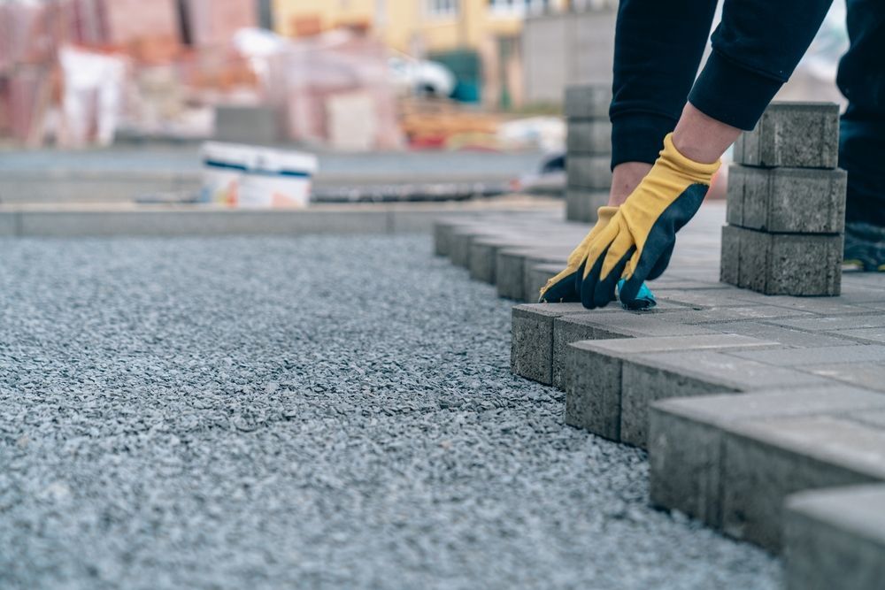 A person wearing yellow gloves is laying bricks on a sidewalk.