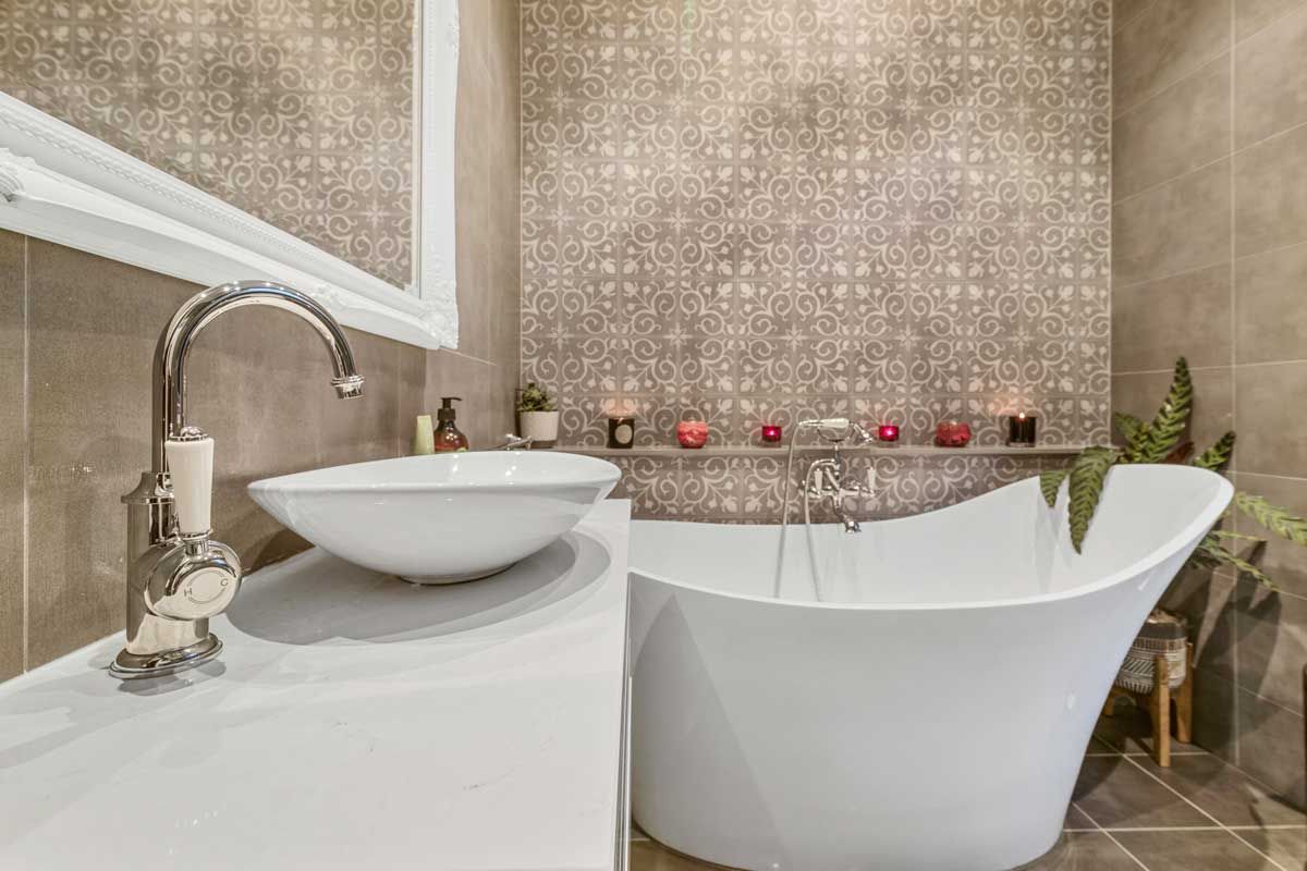 Bathroom renovation with a patterned feature wall, white slipper bathtub, vessel sink, and chrome gooseneck tap.