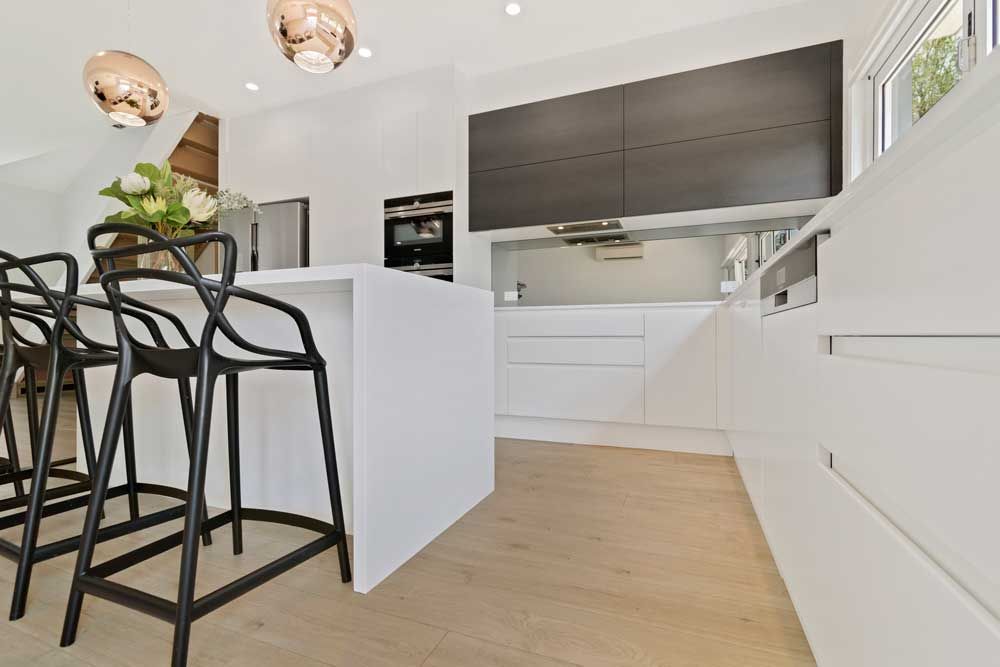 Modern kitchen renovation with a white waterfall island, black bar stools, copper pendant lights, and a mirrored splashback.