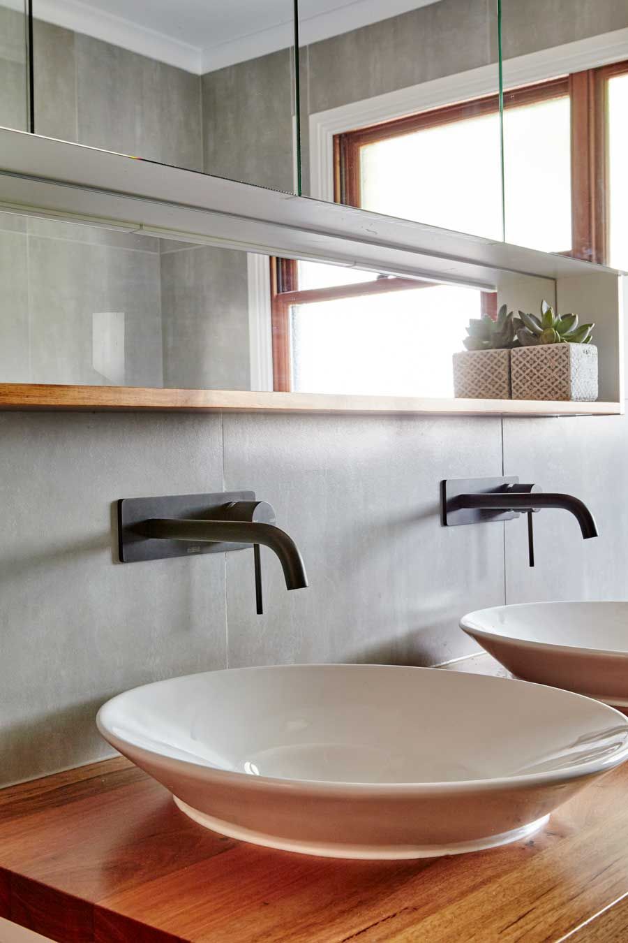 Contemporary double vanity renovation featuring black minimalist faucets, oval vessel sinks, and a wood shelf under a mirrored cabinet