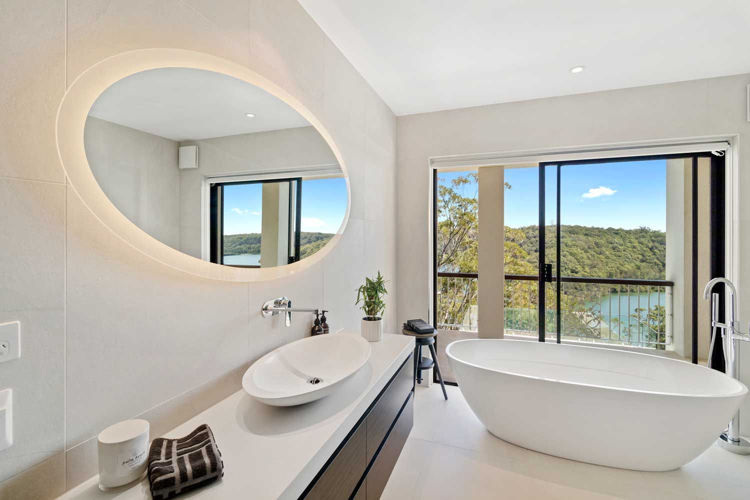 Luxury bathroom renovation featuring a white stone countertop, wall-mounted tap, and soaking tub with a scenic water view.
