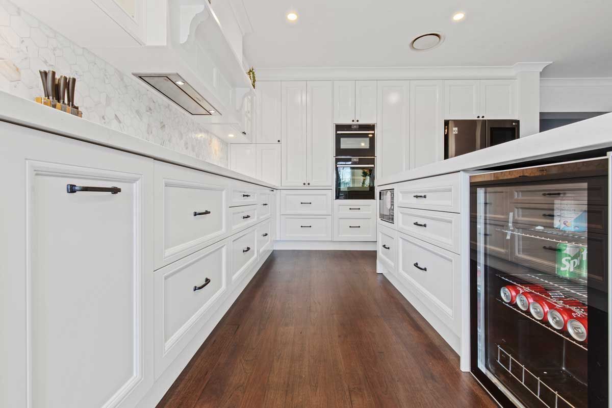 Kitchen renovation with white shaker-style drawers, black handles, integrated wine fridge, and marble hexagonal backsplash.