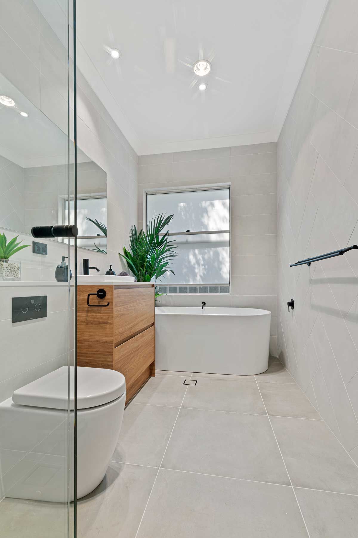 Bright modern bathroom renovation with a freestanding oval tub, timber vanity, and large-format gray floor tiles.