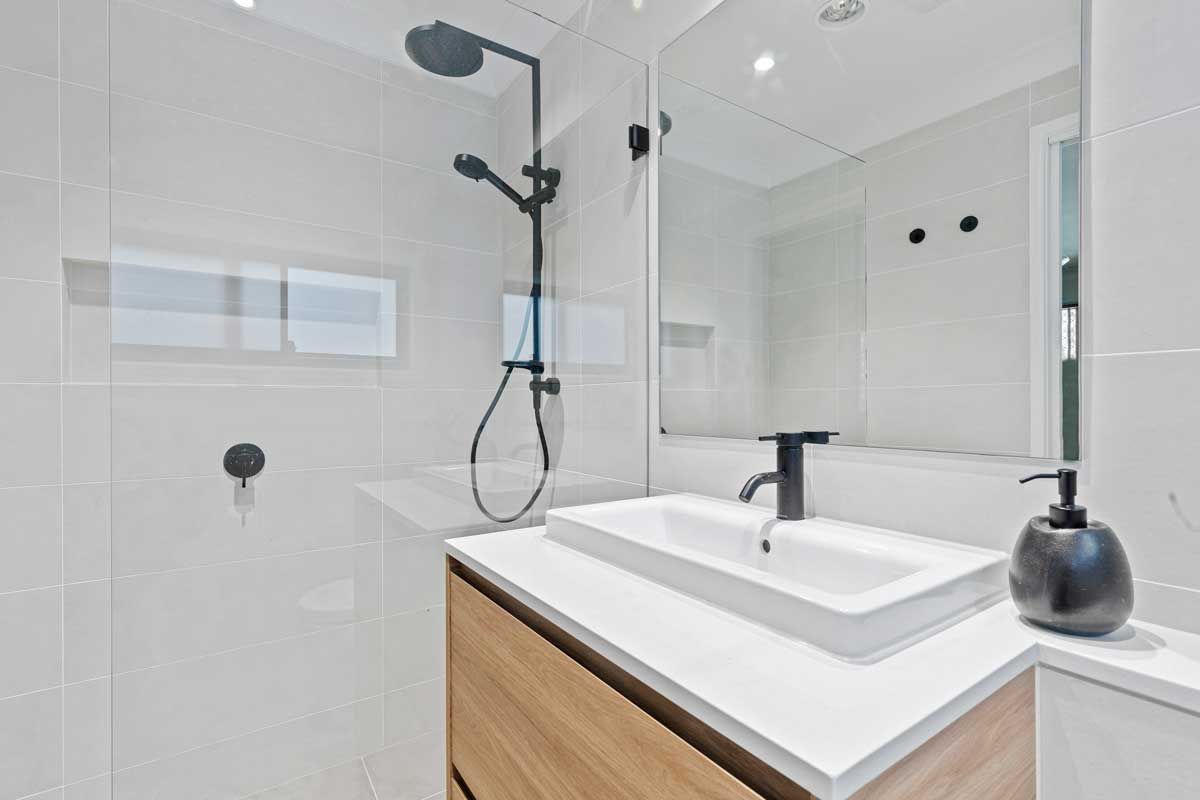Bright white bathroom with wood-grain vanity, matte black fixtures, and large frameless mirror. 