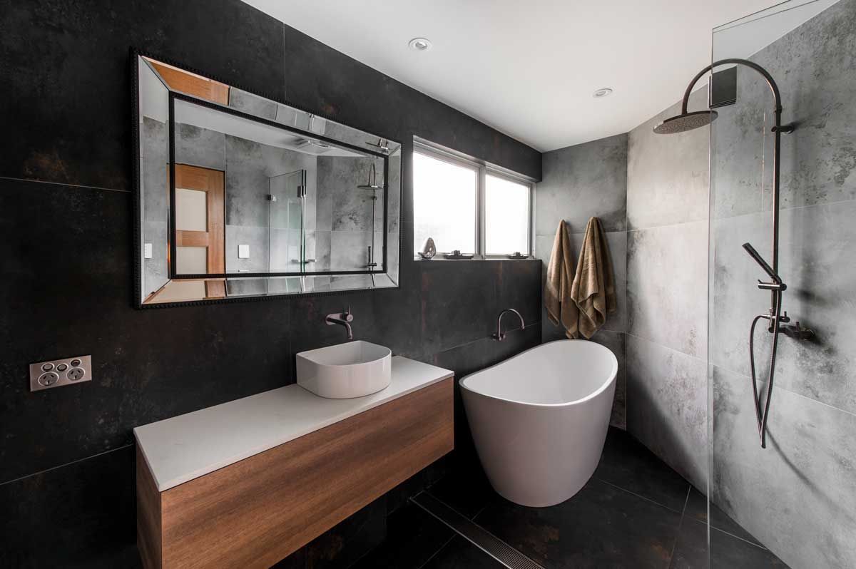 Contemporary bathroom renovation featuring a textured stone-look shower, vessel sink, and large framed mirror over a wood vanity.
