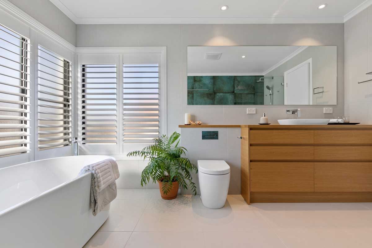 Modern bathroom renovation with a white freestanding bathtub, timber vanity, and white plantation shutters.