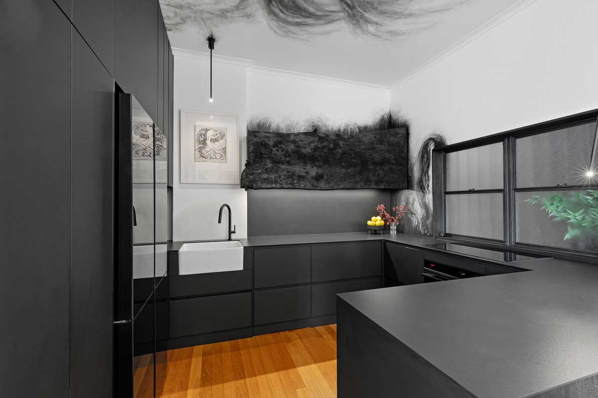 Modern kitchen renovation with matte black cabinetry, white apron-front sink, black gooseneck tap, and abstract smoke-effect wall mural.