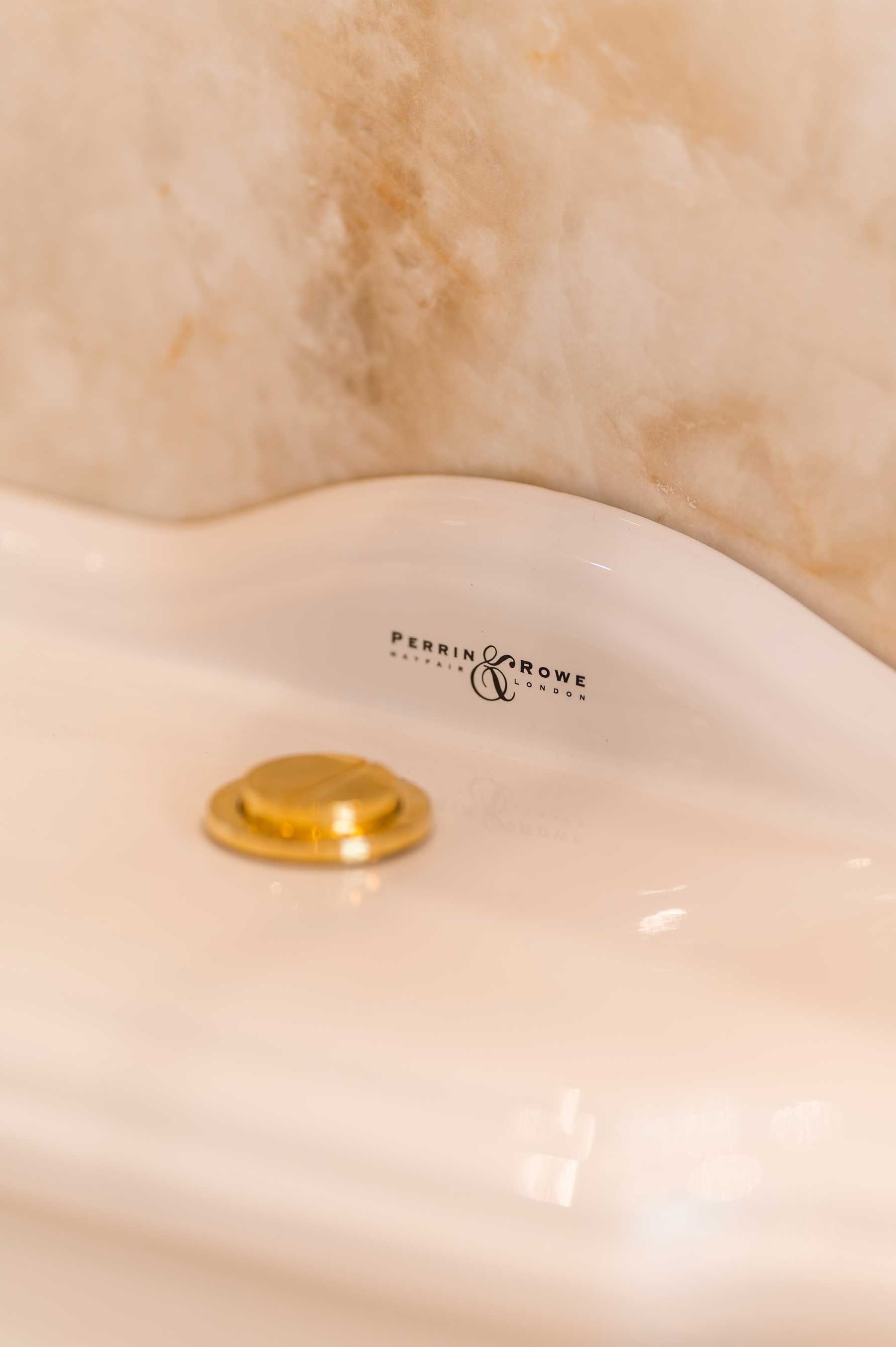 Close-up of a Perrin & Rowe porcelain sink with gold brass hardware and a marble backsplash in a luxury bathroom renovation.