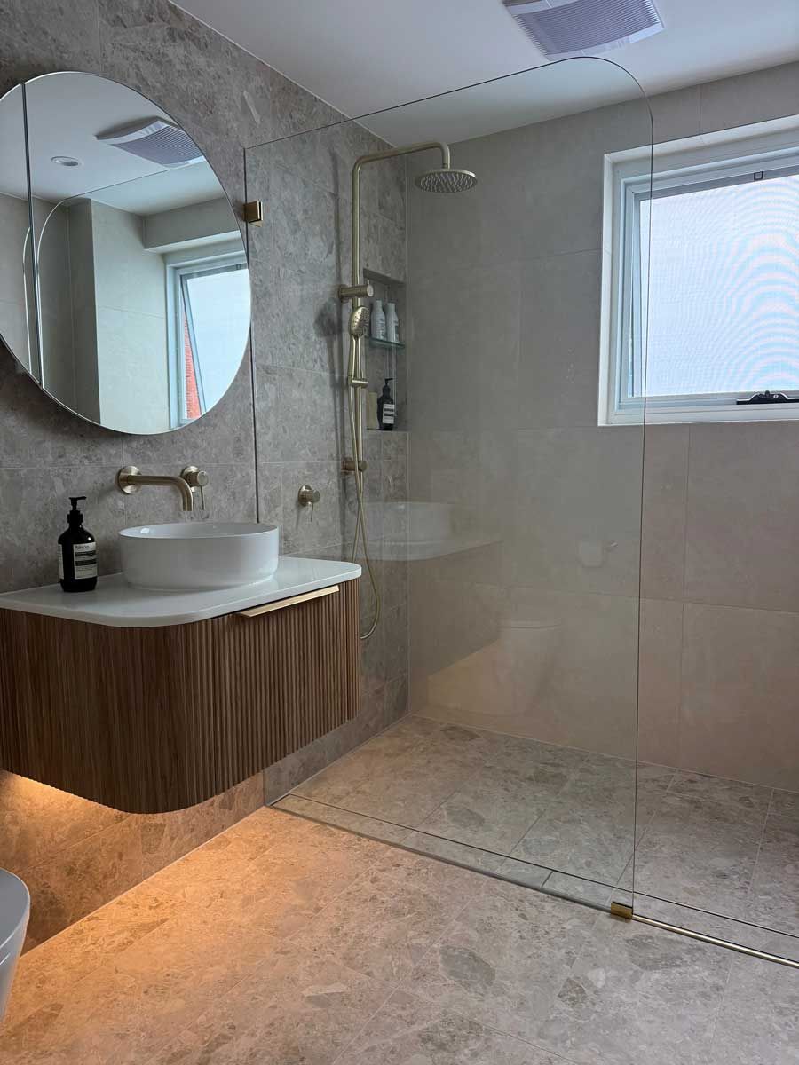 Luxury ensuite renovation featuring a floating timber vanity, vessel sink, and frameless glass shower with stone floor tiles. 