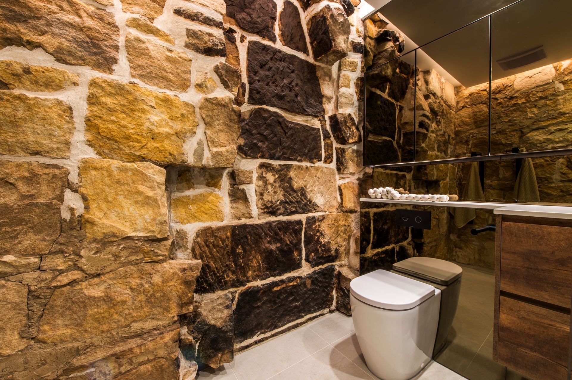 Bathroom renovation with original exposed sandstone walls, a floating timber vanity, white toilet, and backlit LED mirror.