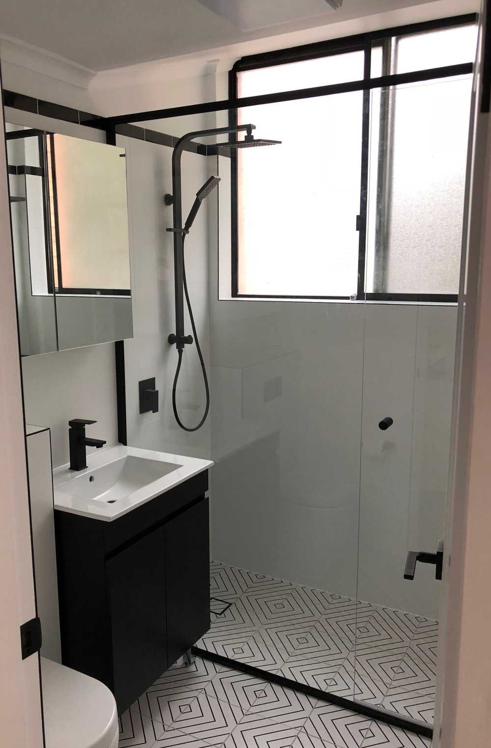 Modern bathroom with black-framed glass shower, matte black fixtures, floating vanity, and geometric patterned floor tile.