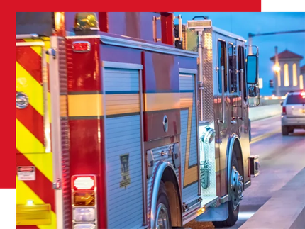 A side view of a red and blue fire engine parked on a bridge during twilight, with a car visible in the distance.
