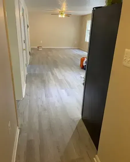 Hallway leading to a living room with light gray flooring. A black appliance is on the right.