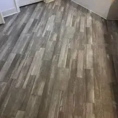 Gray, weathered-look wood plank flooring in a room corner, angled view.