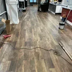 Wooden-look flooring installed in a room. Paint can, tools, and a power cord on the floor.
