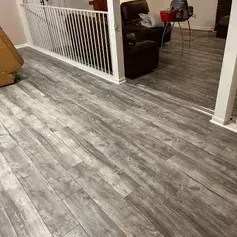 Gray wood-look flooring extends throughout a room. A white railing and brown leather recliner are visible.