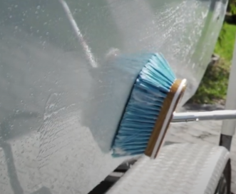 Scrubbing hull of white boat with blue scrub brush.
