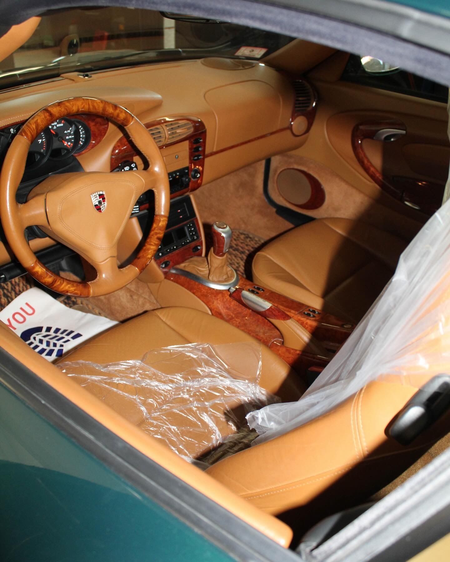 Tan leather Porsche interior with wood trim, covered seats. Steering wheel visible, door open.