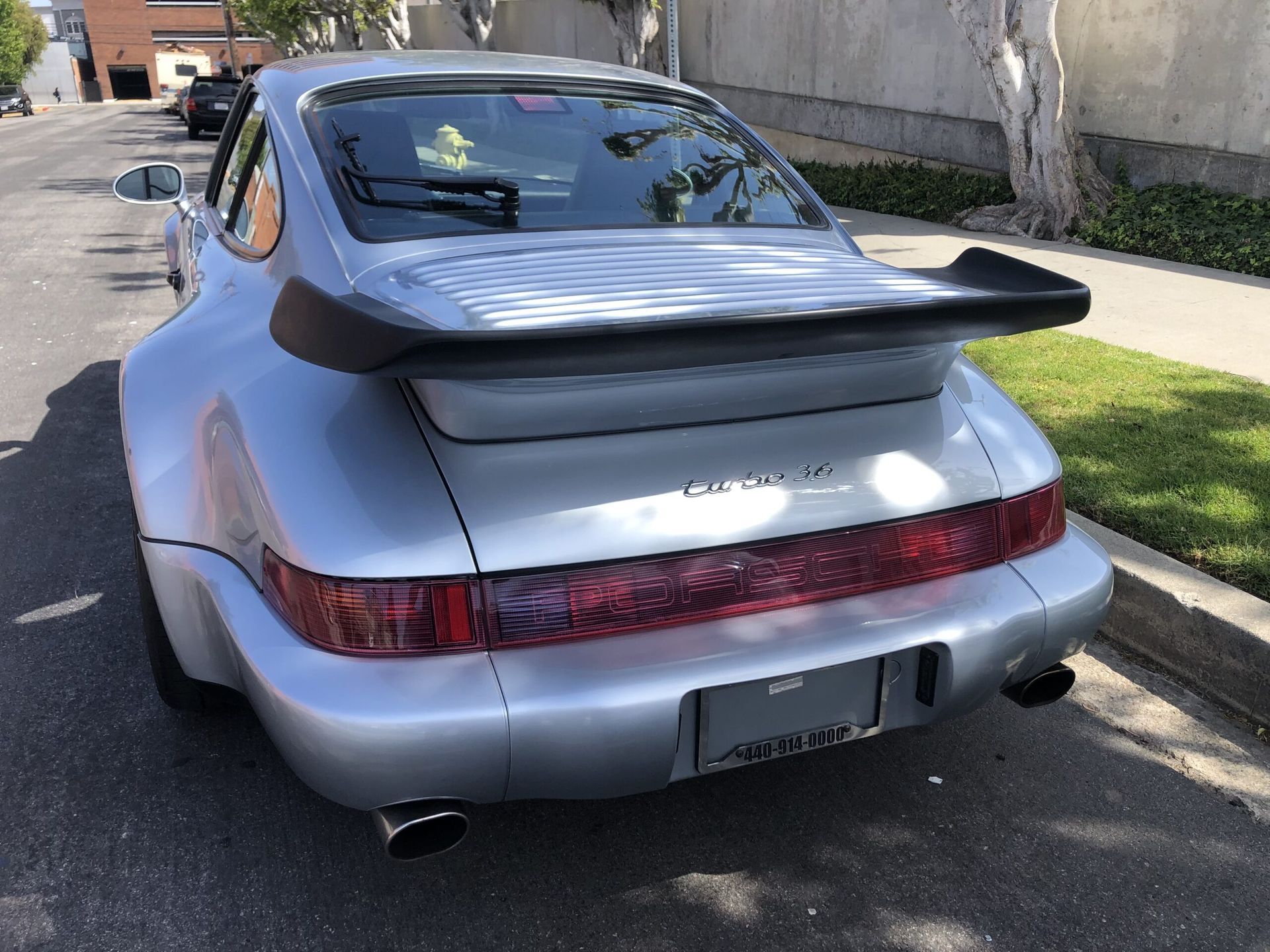 Silver Porsche 911 coupe parked on street with spoiler, rear view.