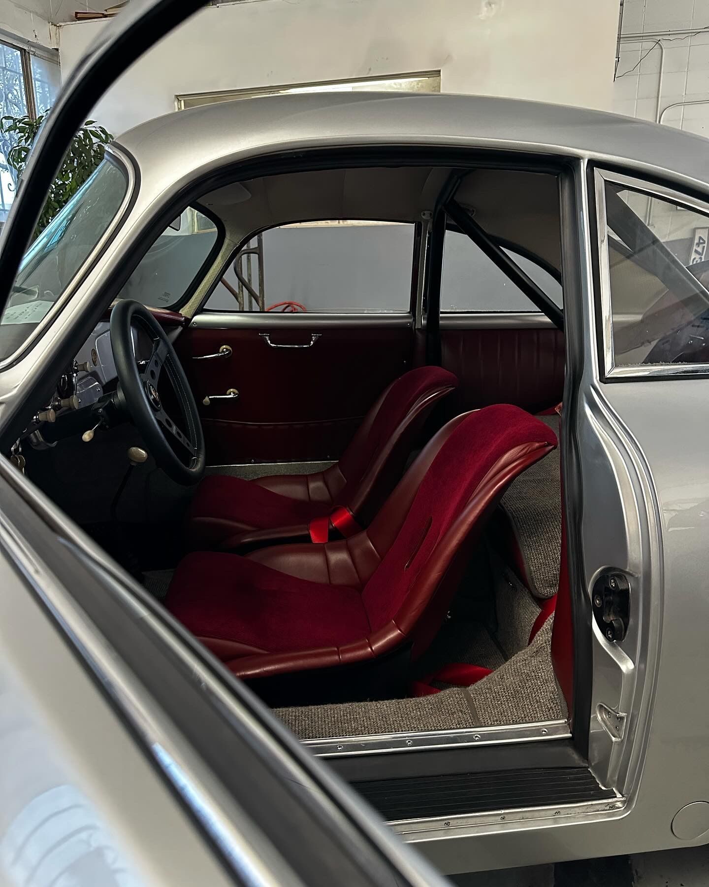 Silver classic car interior with red racing seats and roll cage.