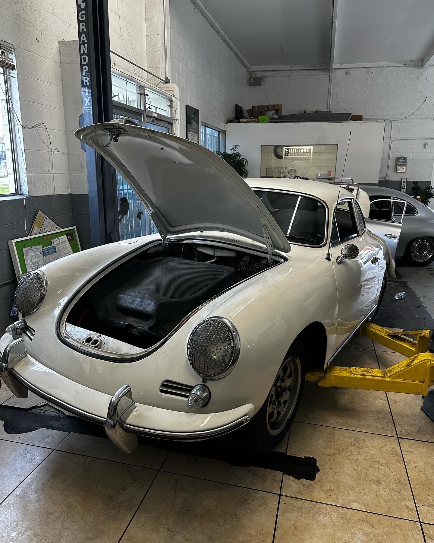 White vintage Porsche with hood open, on a lift inside a garage.