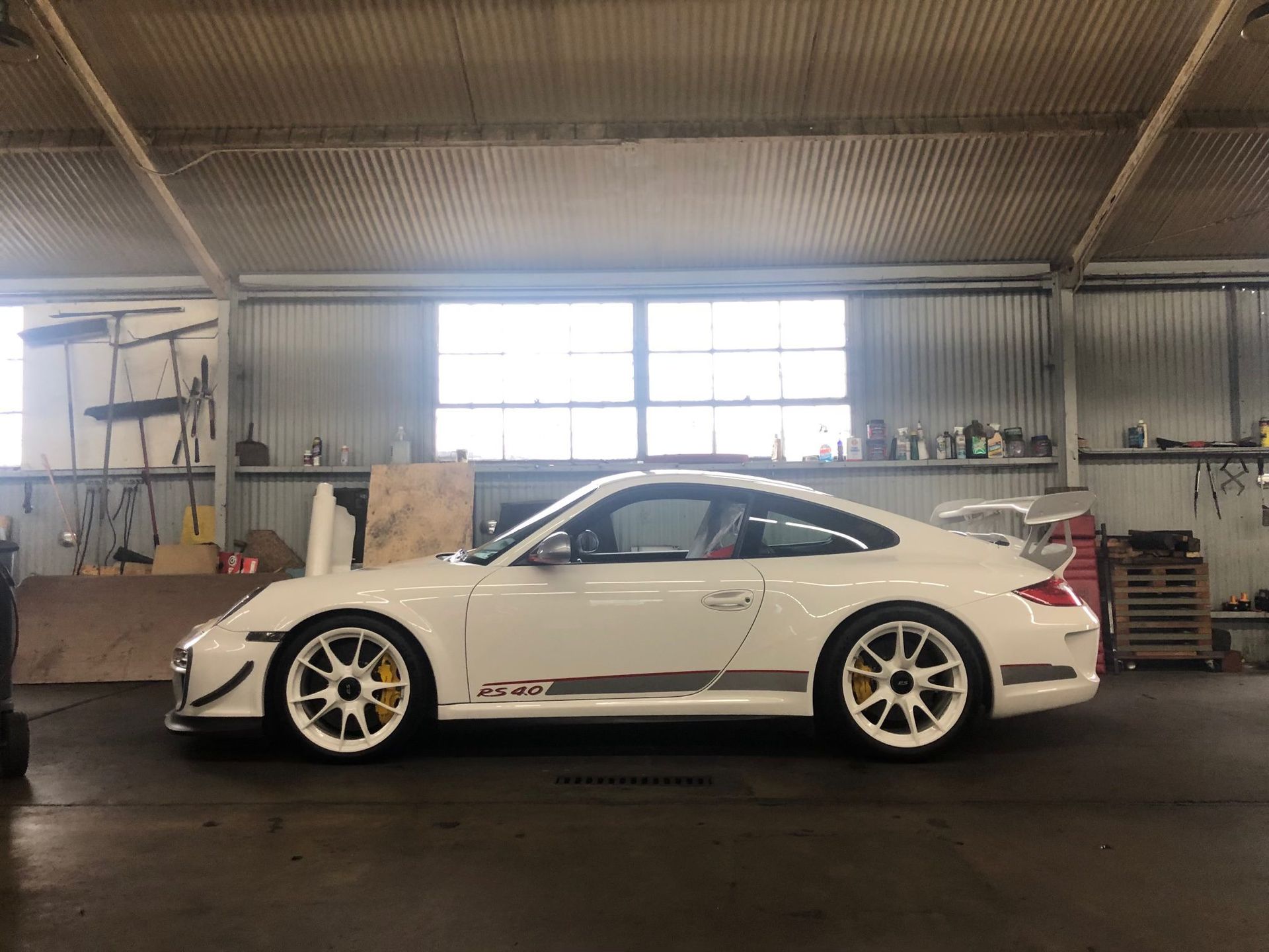 White Porsche 911 GT3 RS in a garage, yellow brake calipers, white wheels, side view.