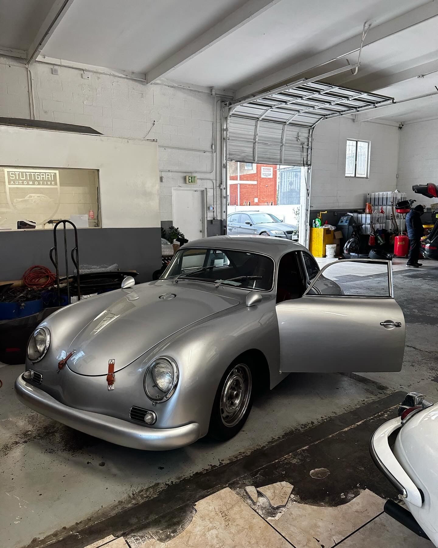Silver vintage Porsche 356 coupe with door open, parked in a garage.