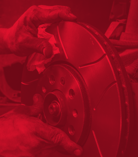 Hands holding a slotted brake rotor during a car repair, tinted red.