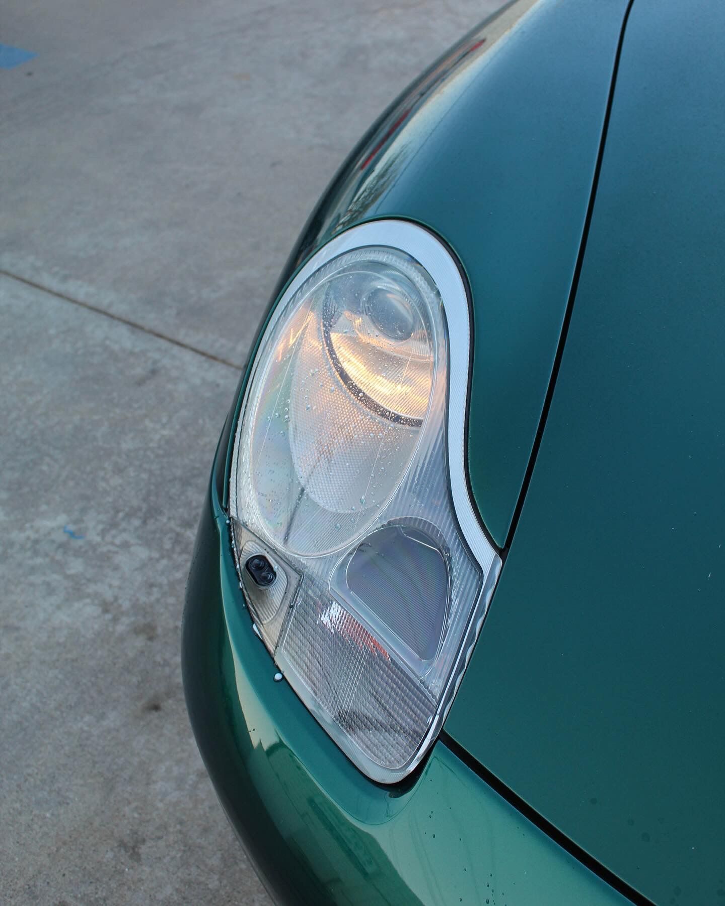 Green car headlight, wet with water droplets, reflecting light.