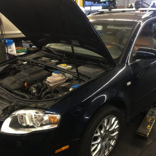 A dark blue car with its hood open in a repair shop. The engine is visible.