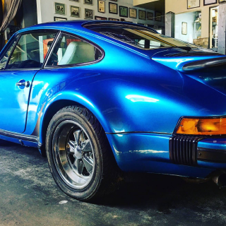 Blue vintage Porsche sports car, shiny paint, parked indoors, bright lighting.