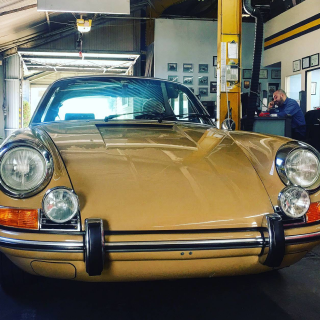 Tan classic Porsche in a repair shop.