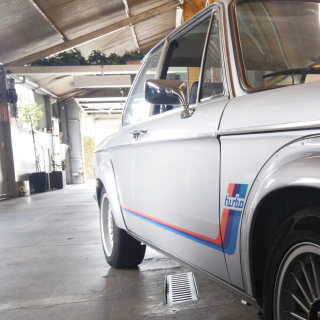 Silver BMW 2002 Turbo with blue, red stripes and Turbo emblem parked in a garage.