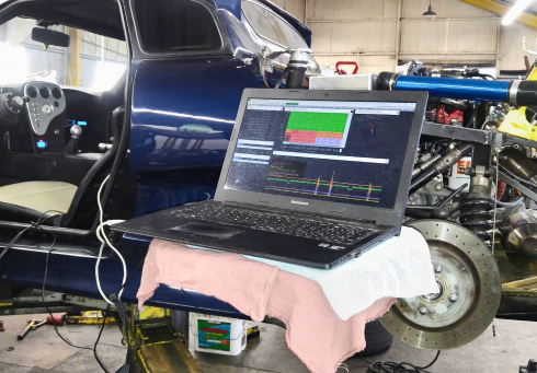 Laptop displaying engine diagnostics data, connected to a blue car's engine.