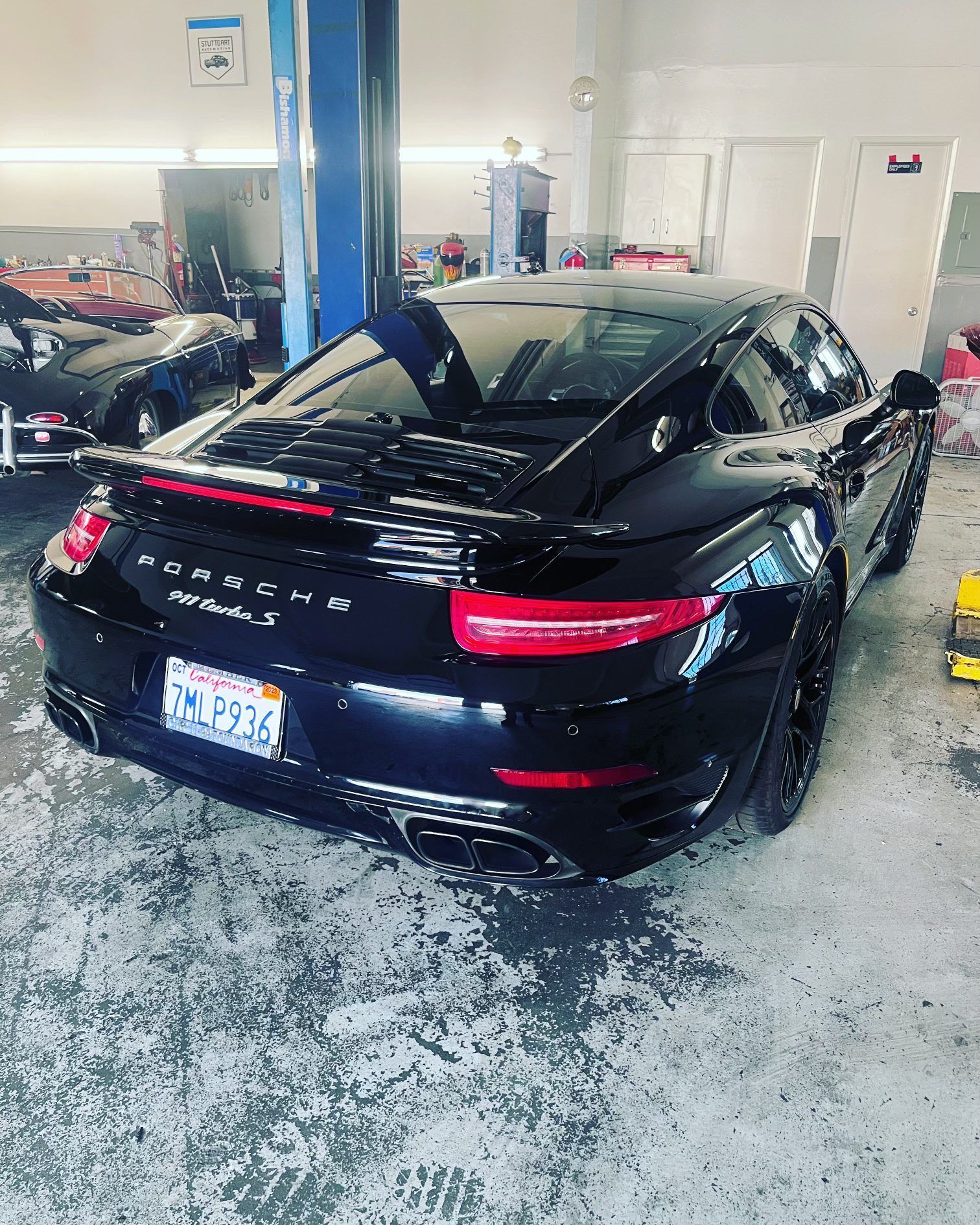 Black Porsche 911 in a garage, California license plate, gray floor, blue lift.