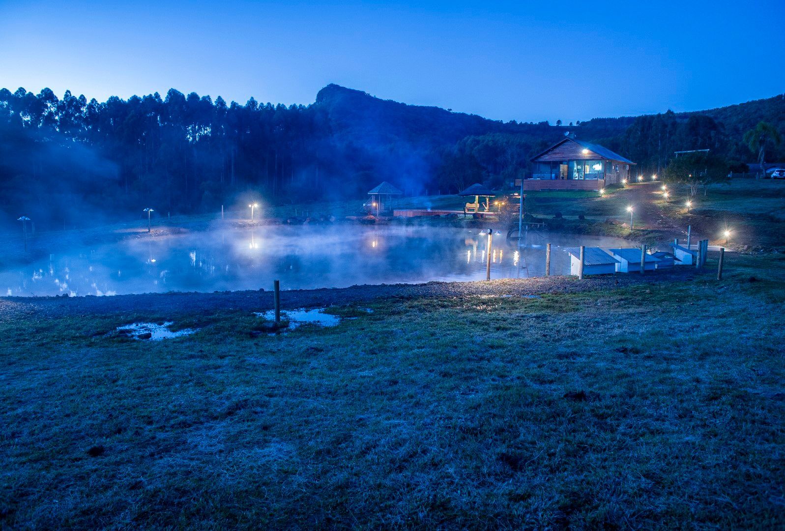 Um grande corpo de água com uma casa ao fundo à noite.