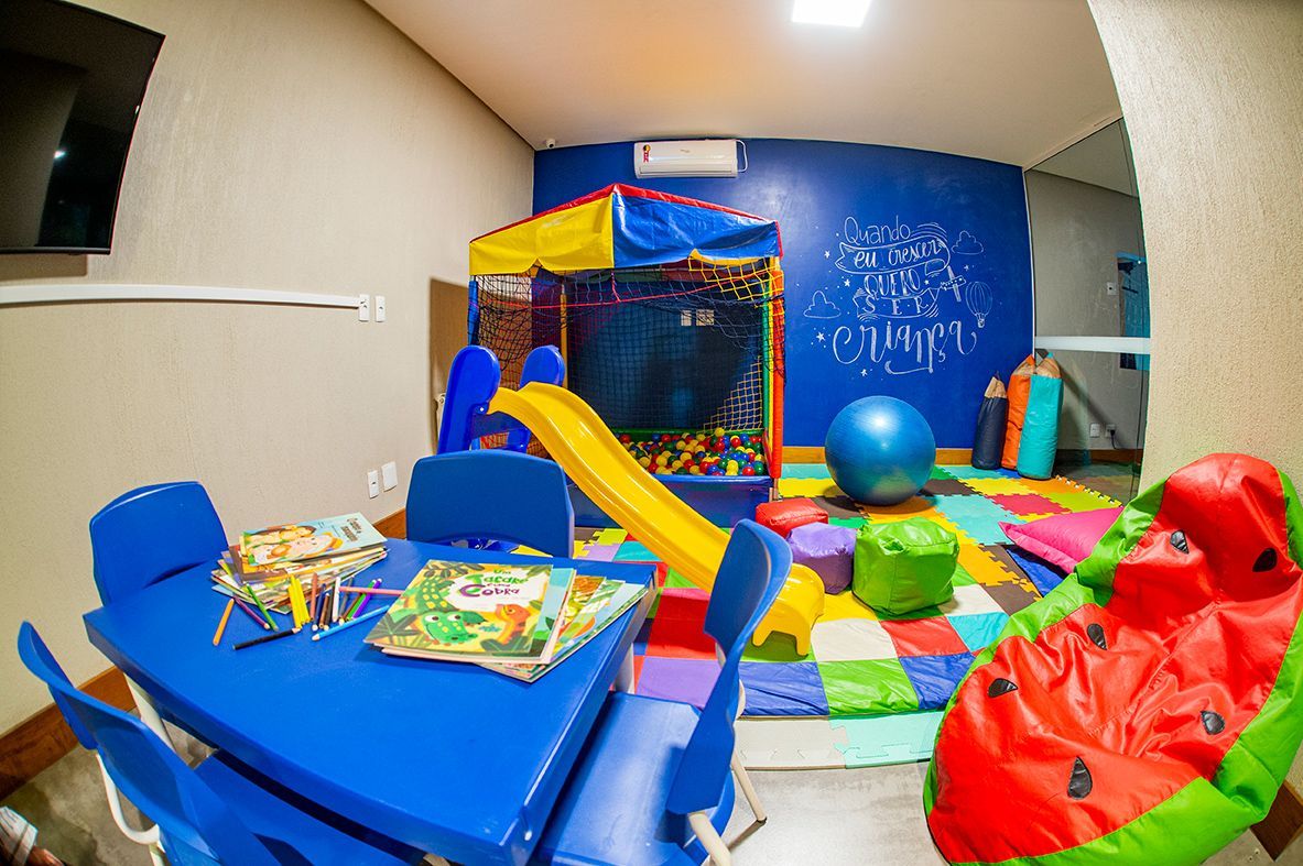 Uma sala de jogos para crianças com mesas, cadeiras, um escorregador e uma cadeira tipo pufe em formato de melancia.