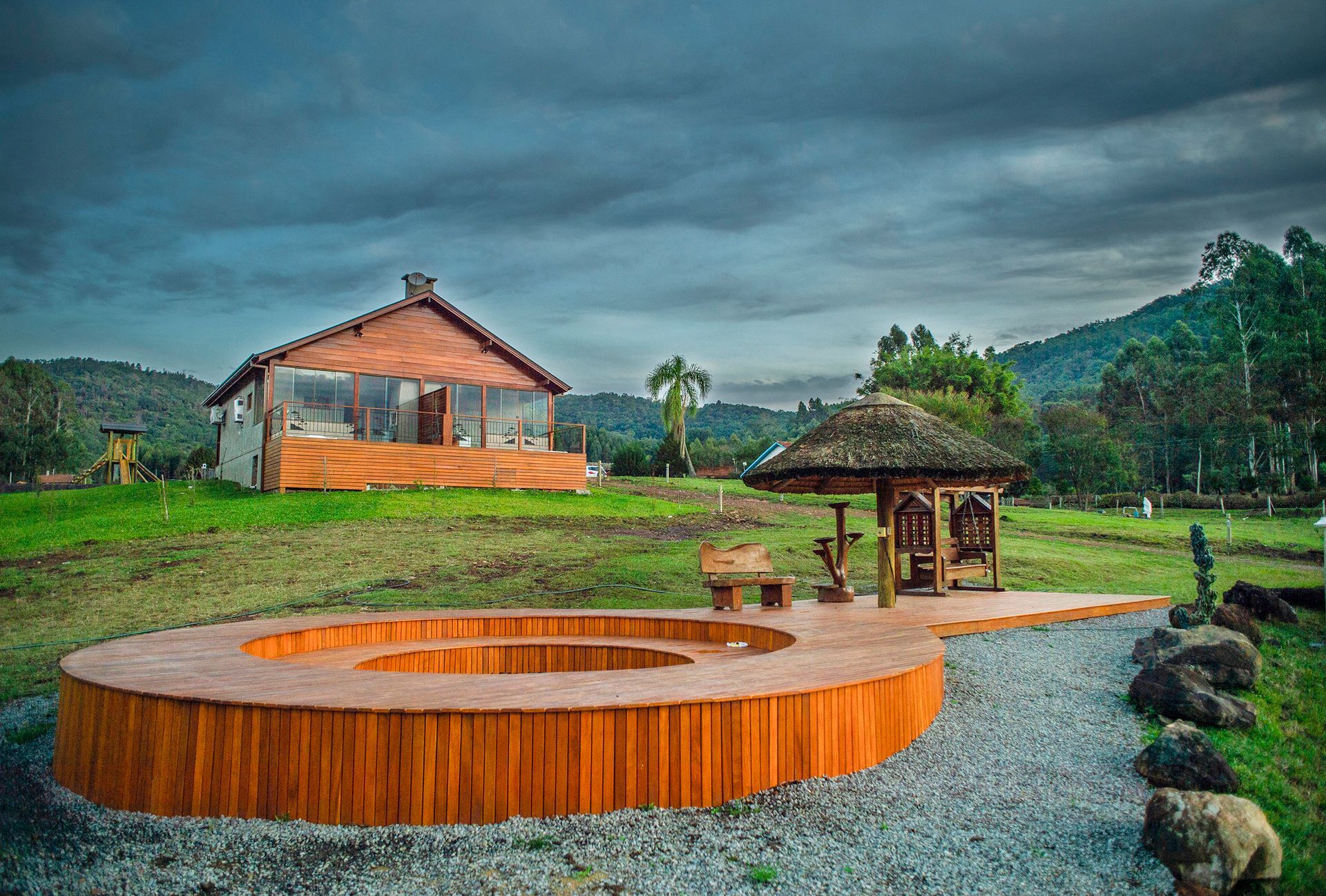 Um gazebo de madeira está situado no meio de um campo gramado em frente a uma casa.